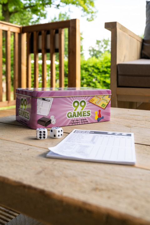 Spilæske med 99 Games, terninger og scoreblok på et havebord ved en safaritelts terrasse, Camping Si-Es-An.
