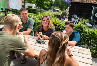 En familie sidder udenfor ved et bord og nyder is ved en safari-teltcampingplads i Holland.