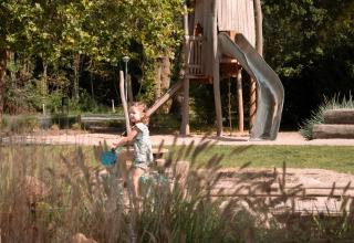 Un niño anda en bicicleta en un parque con un gran tobogán de madera en Camping Si-Es-An, Países Bajos.