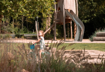 Un niño anda en bicicleta en un parque con un gran tobogán de madera en Camping Si-Es-An, Países Bajos.