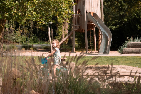 Un enfant fait du vélo dans un parc devant une grande aire de jeux en bois au Camping Si-Es-An, Pays-Bas.