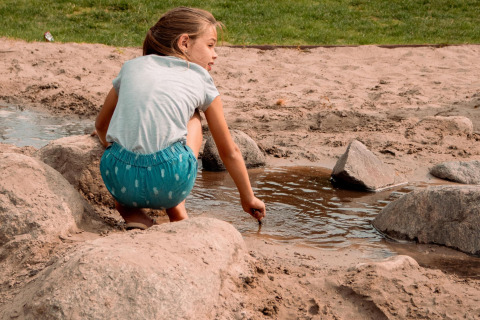 Una niña juega en la arena con agua y rocas en una tienda safari en Camping Si-Es-An, Países Bajos.