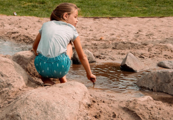 Una niña juega en la arena con agua y rocas en una tienda safari en Camping Si-Es-An, Países Bajos.