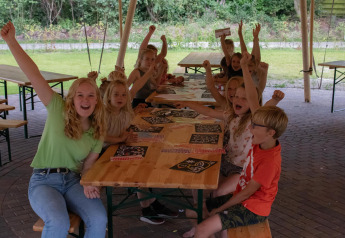 Niños y adultos animan y hacen manualidades juntos bajo una tienda safari en Camping Si-Es-An, Países Bajos.