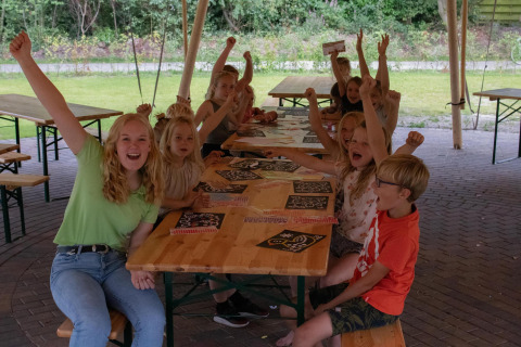 Niños y adultos animan y hacen manualidades juntos bajo una tienda safari en Camping Si-Es-An, Países Bajos.