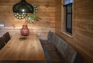 Eethoek in een tiny house met houten wanden, houten tafel, bruine stoelen en grote roze vaas bij Sandberghe.