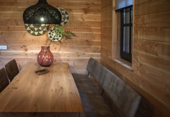 Comedor en una tiny house con paredes de madera, mesa de madera, sillas marrones y un gran jarrón rosa en Sandberghe.