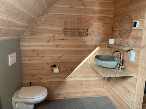 Baño moderno con paredes de madera, inodoro suspendido, lavabo de piedra, espejo y estantes.