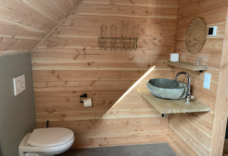 Baño moderno con paredes de madera, inodoro suspendido, lavabo de piedra, espejo y estantes.