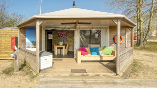 Buitenaanzicht van het Dune house lodge in Marina Parcs Almere, Nederland, met kleurrijke kussens op de bank.