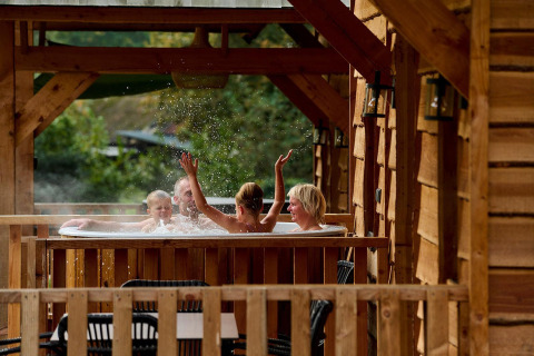 Familia disfruta de un jacuzzi en el porche de madera del lodge Heydehuis en Sandberghe, Países Bajos.