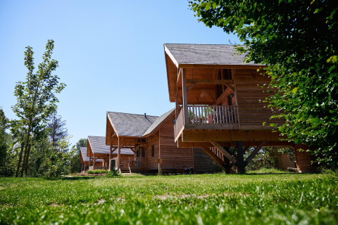 Houten lodges bij Heydehuis + Jacuzzi op Sandberghe, Nederland, tussen bomen en groene grasvelden.