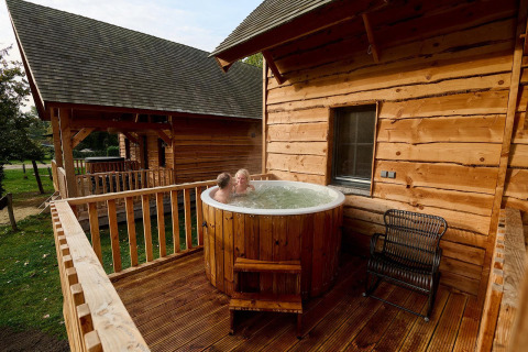 Twee mensen genieten van een buitenjacuzzi op het houten terras van Heydehuis-lodge in Sandberghe, Nederland.