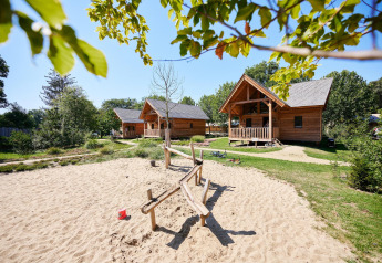 Wooden lodges at Sandberghe in the Netherlands with playground and sandpit, surrounded by greenery and trees.
