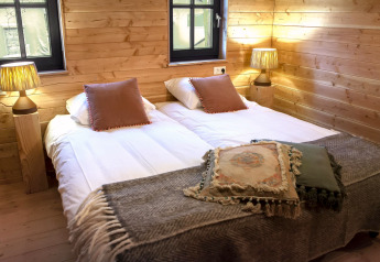 Cozy bedroom at Heydehuis + Jacuzzi glamping with twin beds, wood-paneled walls, warm lighting and lamps.