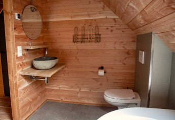 Wood-paneled bathroom with stone basin, round mirror, and toilet at glamping accommodation Heydehuis + Jacuzzi.
