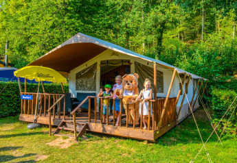 Niños y una mascota de oso en la terraza de una tienda safari en Lodgetent Beaufort, Holiday Park Walsdorf, Luxemburgo.