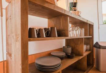 Estantería de madera con vajilla y cafetera en la tienda Lodgetent Beaufort, Beter Uit Holiday Park Walsdorf.