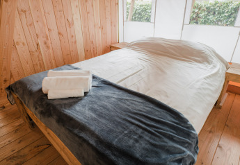Interior de una tienda safari Lodgetent Beaufort con cama hecha y toallas limpias en Beter Uit Holiday Park Walsdorf en Luxemburgo.