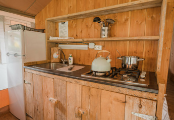 Zona de cocina en una tienda safari lodge con pared de madera, fogón de gas, hervidor y fregadero.
