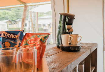 Cafetera con dos tazas, snacks y vasos sobre mesa de madera en tienda safari en Beter Uit Holiday Park Walsdorf.