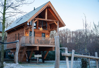 Treehouse on stilts with balcony and stairs at Sandberghe in the Netherlands, surrounded by natural scenery.