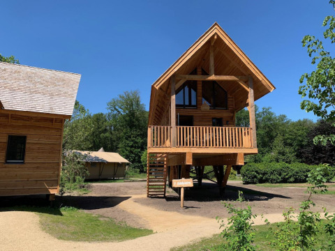 Træhus Heydehuis med jacuzzi ved Sandberghe, Holland, omgivet af træer og blå himmel på en solrig dag.