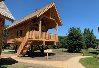 Casa del árbol con balcón y escalera en Sandberghe, Países Bajos, rodeada de árboles y cielo azul.