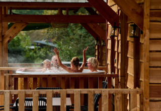 Familie nyder jacuzzi på træhusets terrasse ved Sandberghe i Holland, børn leger med vand.