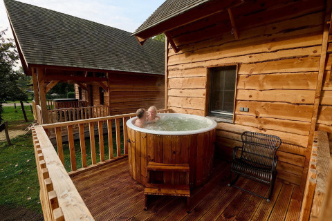 Twee mensen ontspannen in een buitenjacuzzi op het terras van de boomhut Heydehuis bij Sandberghe, Nederland.
