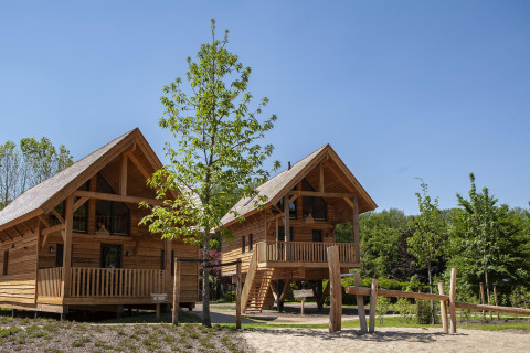 Twee houten boomhutten met jacuzzi bij Sandberghe in Nederland, omgeven door bomen en blauwe lucht.