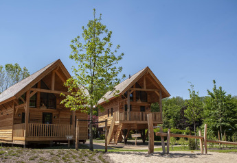 Zwei Baumhäuser mit Jacuzzi im Sandberghe, Niederlande, umgeben von Bäumen und blauem Himmel.