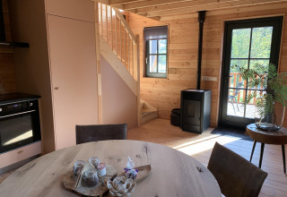 Modernes Baumhaus-Interieur mit Holztreppe, Kamin, Tisch und Ausblick bei Sandberghe in den Niederlanden.