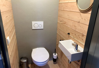 Moderne toiletruimte met houten wanden, kleine wastafel en ronde spiegel in Heydehuis + Jacuzzi, Sandberghe, Nederland.
