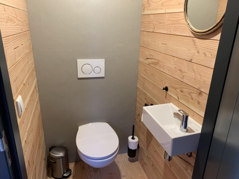 Moderne toilet med trævægge, lille håndvask og rundt spejl i Heydehuis + Jacuzzi, Sandberghe, Holland.
