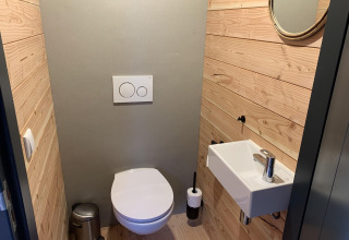 Baño moderno con paredes de madera, lavabo pequeño y espejo redondo en Heydehuis + Jacuzzi, Sandberghe, Países Bajos.