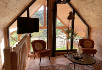 Lys stue i træhus Heydehuis + Jacuzzi ved Sandberghe, Nederlandene, med store vinduer og hyggelig indretning.