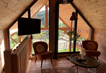 Salon lumineux du Heydehuis + Jacuzzi tree house à Sandberghe, Pays-Bas, avec de grandes fenêtres vitrées.