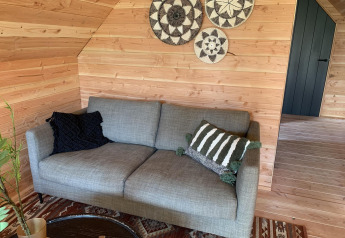 Grå sofa med pyntepuder, vægdekorationer og træpaneler i et hyggeligt sommerhus, Sandberghe, Holland.