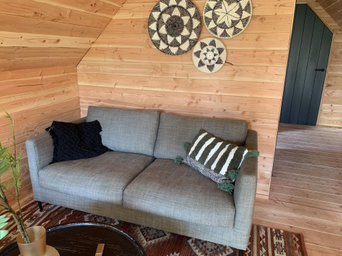 Grå sofa med pyntepuder, vægdekorationer og træpaneler i et hyggeligt sommerhus, Sandberghe, Holland.