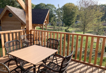 Wooden terrace with table and chairs overlooking greenery at Heydehuis + Jacuzzi, Sandberghe, Netherlands.
