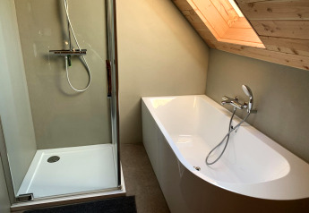 Moderne badeværelse med bruser og badekar under et skråt loft i et træhus på Heydehuis, Sandberghe.