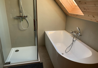 Moderne badeværelse med bruser og badekar under et skråt loft i et træhus på Heydehuis, Sandberghe.