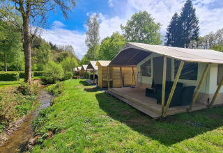 Tiendas tipo safari Lodge junto a un arroyo en Beter Uit Holiday Park Walsdorf, Luxemburgo, rodeadas de naturaleza.