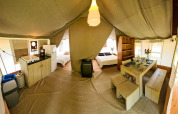 Vista interior de una tienda safari lodge con cocina, mesa de comedor, dos camas y decoración acogedora.
