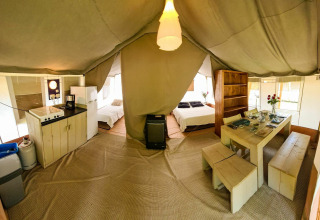 Vista interior de una tienda safari lodge con cocina, mesa de comedor, dos camas y decoración acogedora.
