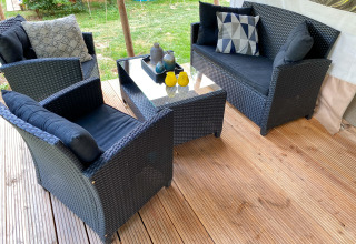 Zona de estar exterior con muebles de mimbre negro y cojines en una terraza de madera en la tienda Eifel.