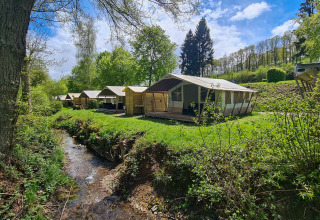 Tiendas tipo safari Lodge en Beter Uit Holiday Park Walsdorf, Luxemburgo, rodeadas de vegetación y un arroyo.