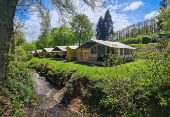 Tiendas tipo safari Lodge en Beter Uit Holiday Park Walsdorf, Luxemburgo, rodeadas de vegetación y un arroyo.