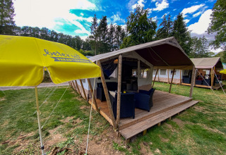 Tienda safari Lodge en Beter Uit Holiday Park Walsdorf, Luxemburgo, con terraza, sillas y sombrilla amarilla.